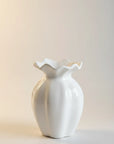 A glossy white ceramic vase with a ruffled, flower-like rim, standing on a neutral light beige background.