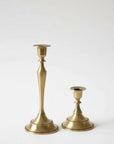 Two brass candlesticks of different heights standing on a light gray background.