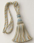 A decorative tassel with a braided cord and a fringed tassel, featuring a muted blue-gray and mustard yellow striped pattern, accented with a beaded band and a gold-toned collar, set against a plain light beige background.