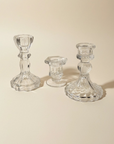 Three clear glass candlestick holders of different heights arranged on a warm beige background.