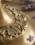 Close-up of a brass ornate mirror with a purple flower on a wooden surface