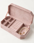 An open dusty pink velvet jewelry box with multiple compartments and a pearl necklace inside, photographed on a clean off-white background.