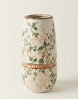 A small cylindrical ceramic vase with a textured off-white glaze, decorated with green botanical vines and delicate peach-pink floral motifs, separated by a rustic terracotta band.