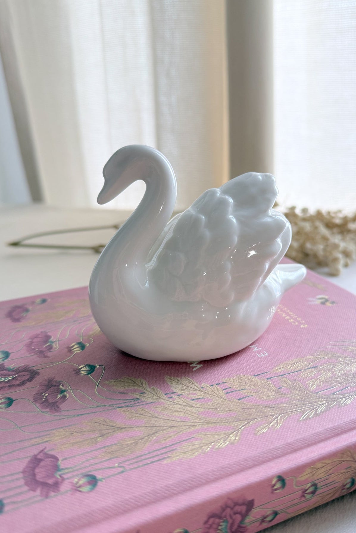 White swan figurine on a pink decorative book with a blurred background