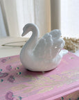 White swan figurine on a pink decorative book with a blurred background