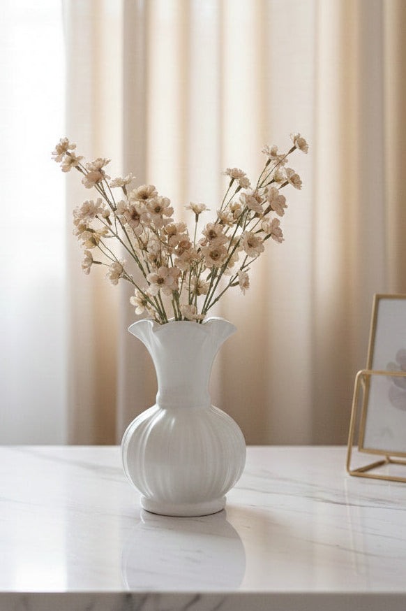 White vase with dried flowers on a marble surface with a neutral curtain background