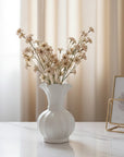 White vase with dried flowers on a marble surface with a neutral curtain background