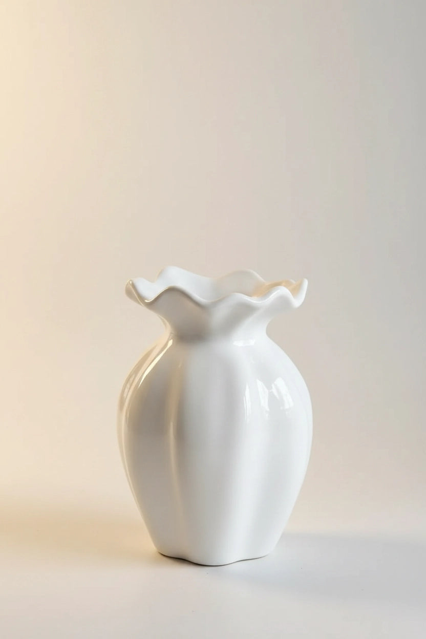 A glossy white ceramic vase with a ruffled, flower-like rim, standing on a neutral light beige background.