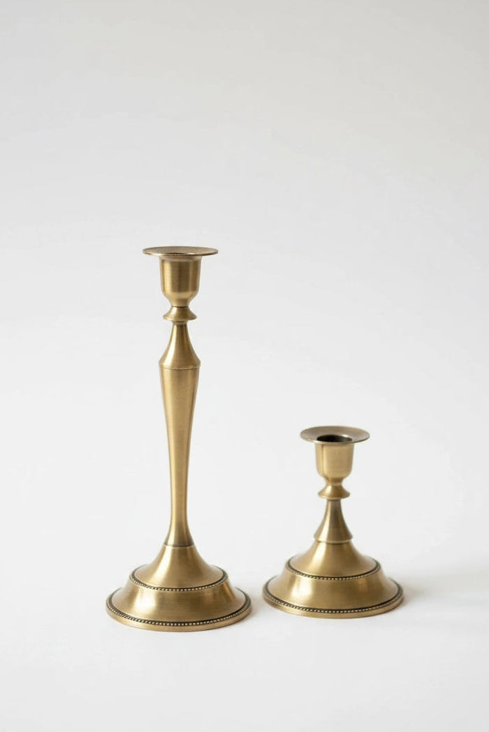 Two brass candlesticks of different heights standing on a light gray background.