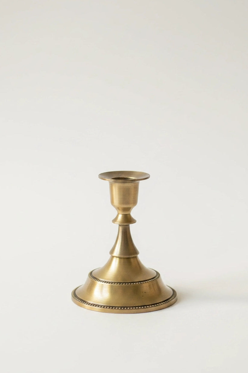 A single brass candlestick holder with a flared base and a simple stem, photographed against a plain light background.