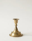 A single brass candlestick holder with a flared base and a simple stem, photographed against a plain light background.