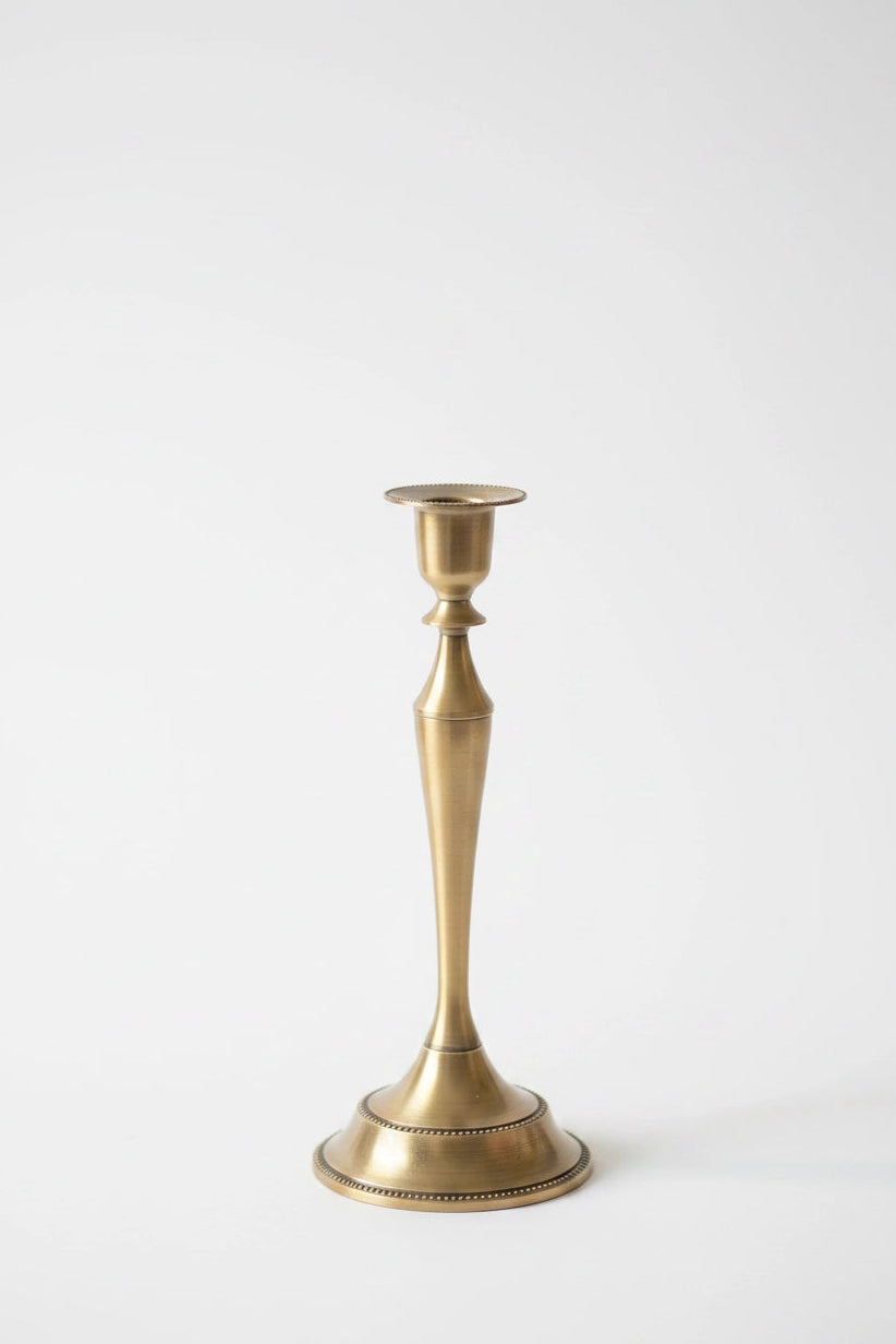 A single brass candlestick holder with a flared base and a slender, tapered stem, shown against a plain white background.