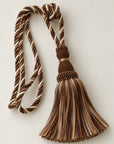 A decorative curtain tassel with twisted braided cords in brown, beige, and cream tones, photographed on a plain light background.