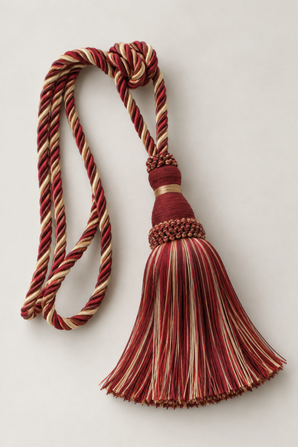 A decorative tassel with a knotted cord loop, featuring striped red, beige, and brown threads, set against a plain light gray background.