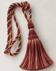 A decorative tassel with a knotted cord loop, featuring striped red, beige, and brown threads, set against a plain light gray background.