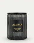 A dark charcoal gray ribbed glass candle jar with a black lid and a black label featuring gold lettering that reads 'ALUMA' and 'Blackberry & Bay'.