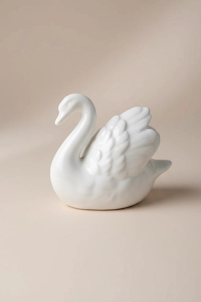 A white ceramic swan figurine with detailed feather and neck carvings, set against a warm beige background with soft shadows.