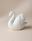 A white ceramic swan figurine with detailed feather and neck carvings, set against a warm beige background with soft shadows.