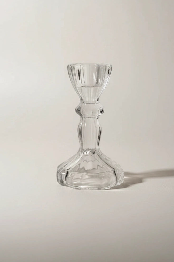 A clear glass candlestick holder with a flared base and a ribbed stem, photographed on a plain light background with a soft shadow.