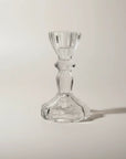 A clear glass candlestick holder with a flared base and a ribbed stem, photographed on a plain light background with a soft shadow.