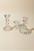 Three clear glass candlestick holders of different heights arranged on a warm beige background.