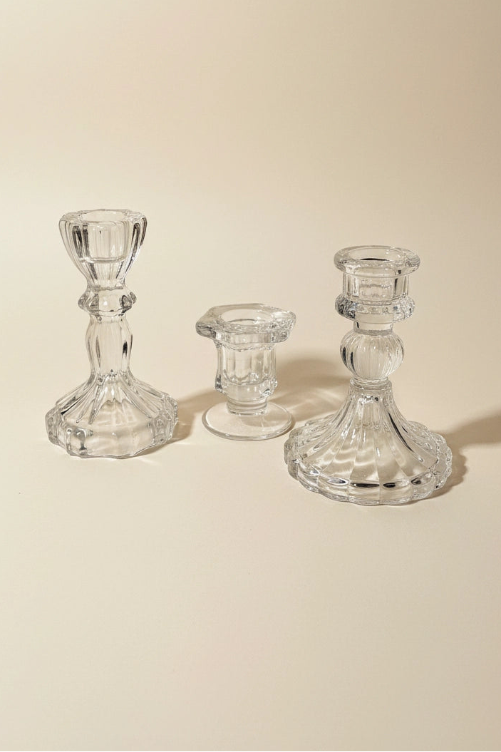 Three clear glass candlestick holders of different heights arranged on a warm beige background.