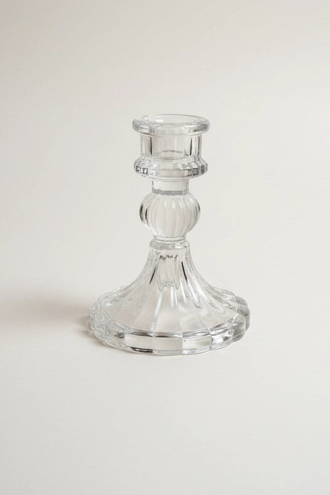 A clear glass candlestick holder with a flared base and a ribbed stem, photographed on a plain light background.