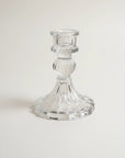 A clear glass candlestick holder with a flared base and a ribbed stem, photographed on a plain light background.