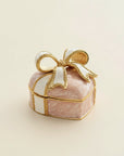 A small decorative gift box for rings  with a pink marbled body, white ribbon, and gold trim, topped with a large bow, photographed on a plain light beige background.