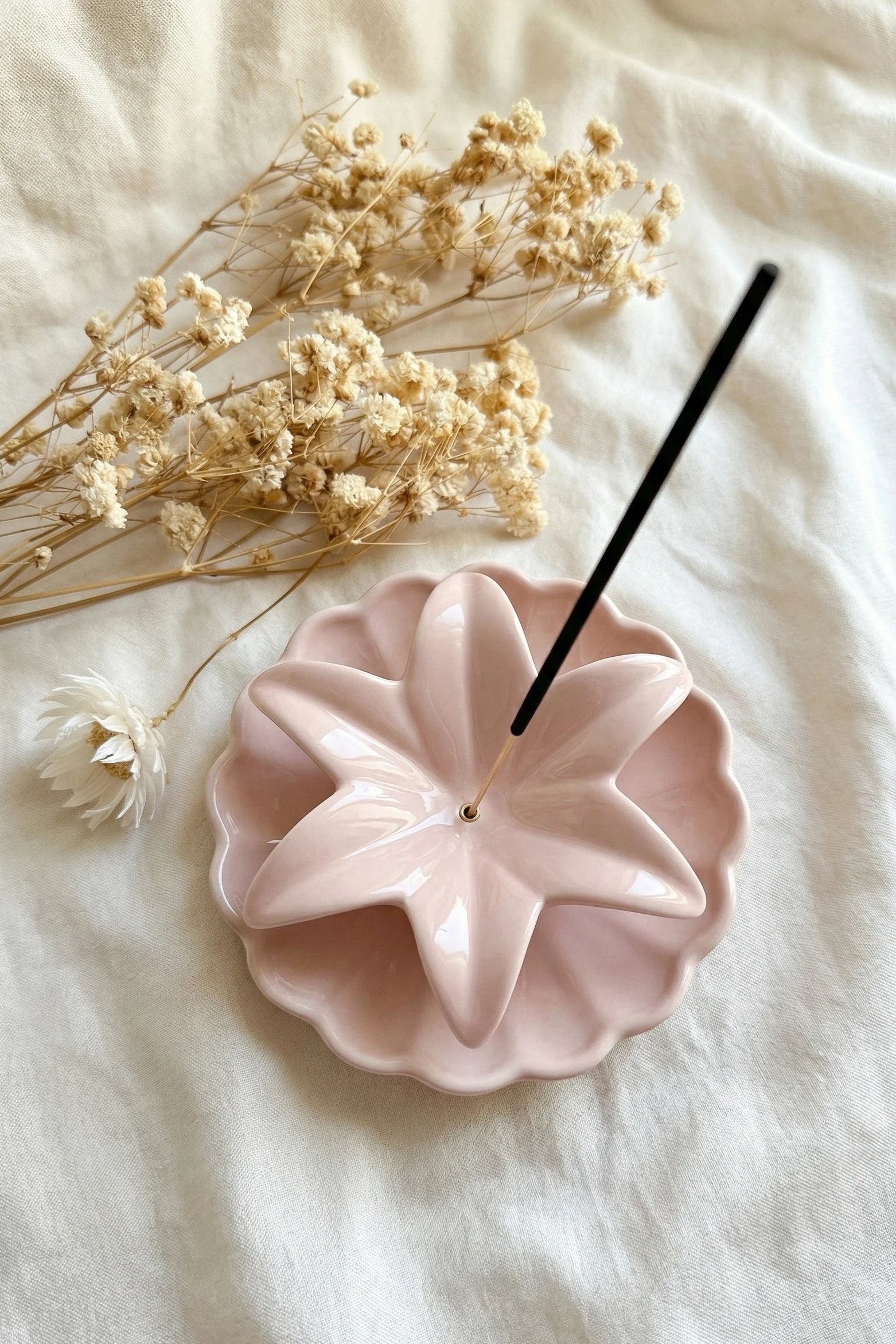 Pink ceramic incense holder with a black incense stick on a white fabric background