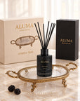 brass tray and black reed defuser bottle sitting on it, on a beautiful marble table with the athean cream gift box and reed defuser box in black, two black berry next to the tray 