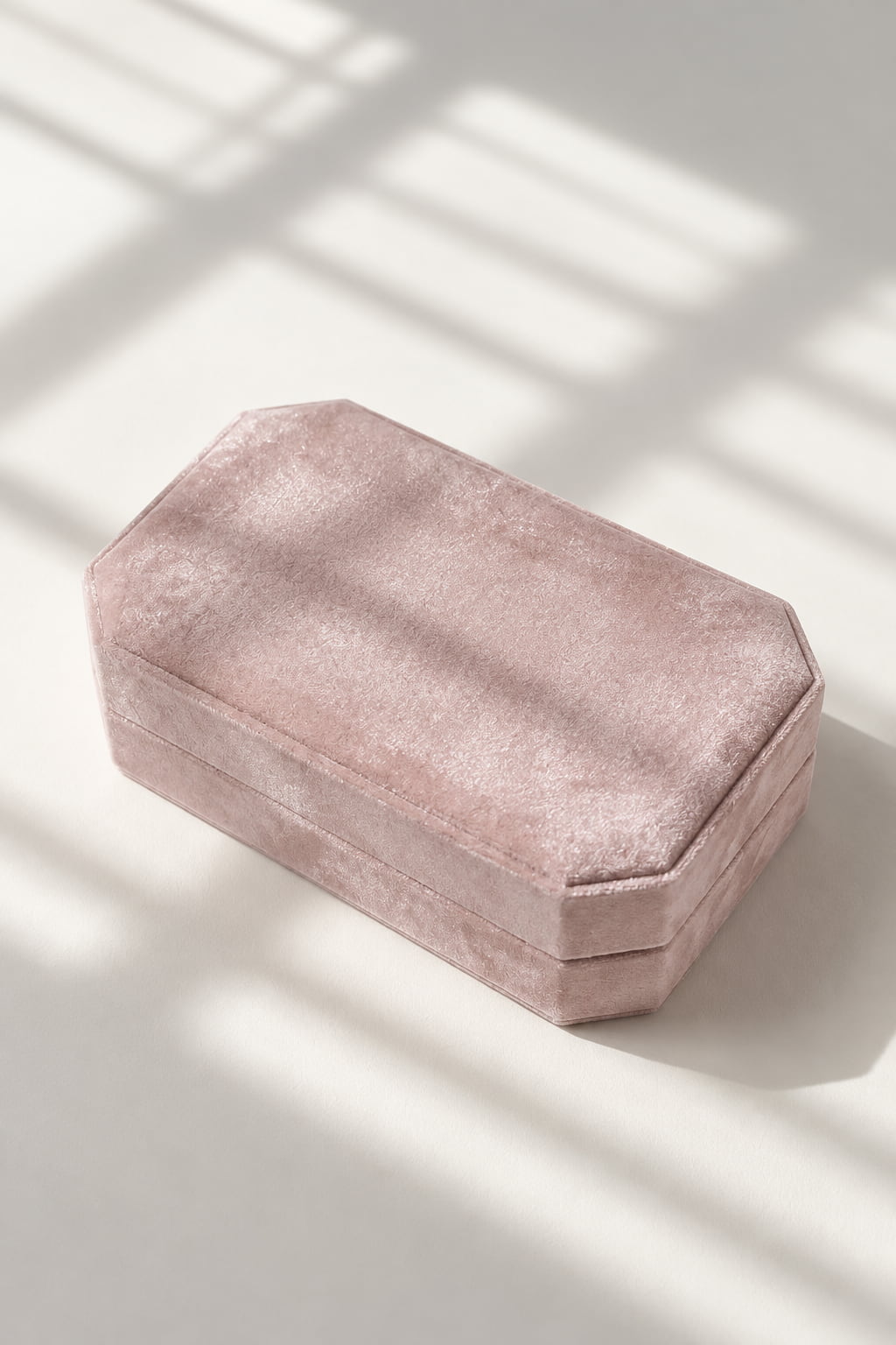 A dusty pink velvet octagonal jewelry box with a textured velvet finish, photographed on a light beige surface with soft window shadow overlays.