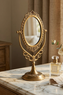 Decorative brass mirror on a marble surface with a bottle of perfume and a white cloth.