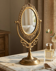 Decorative brass mirror on a marble surface with a bottle of perfume and a white cloth.