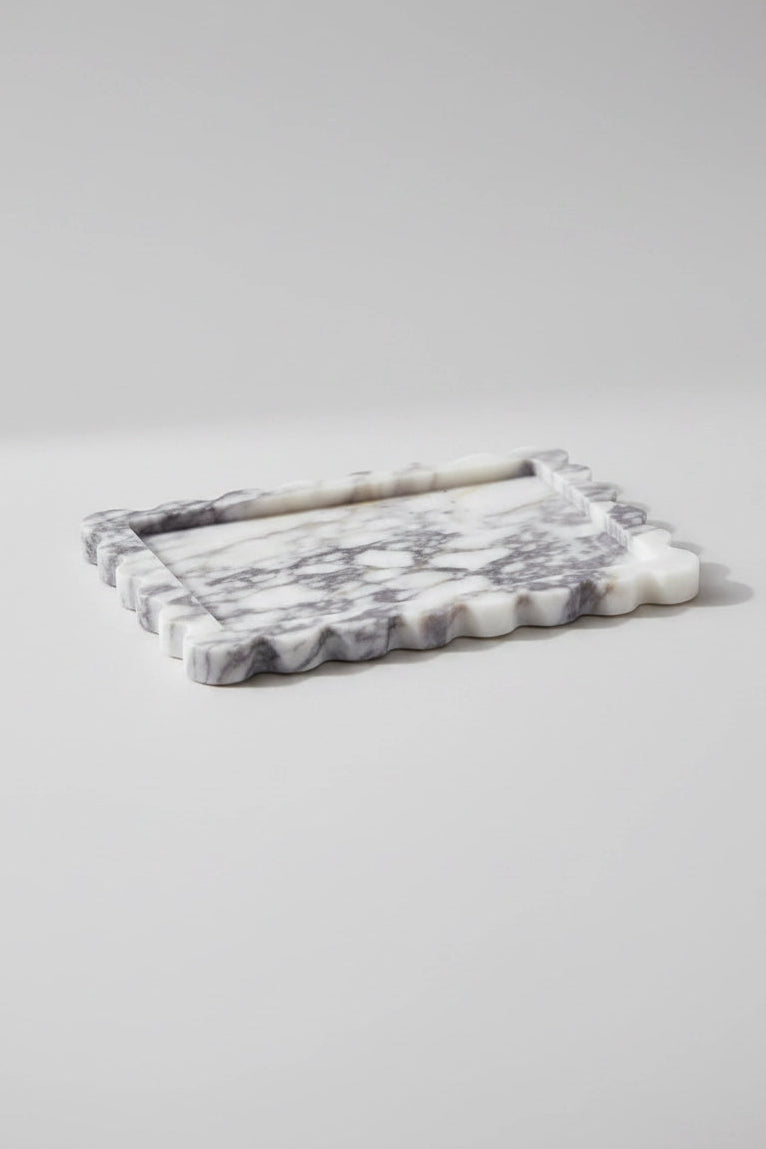 A rectangular marble tray with a scalloped wavy edge, featuring a white and gray marbled pattern, photographed on a neutral light gray background.