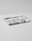A rectangular marble tray with a scalloped wavy edge, featuring a white and gray marbled pattern, photographed on a neutral light gray background.
