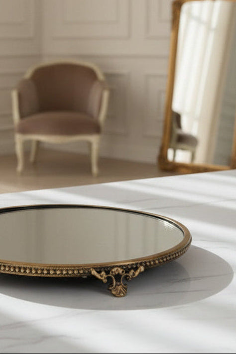 Decorative round mirror with brass frame on a marble surface, blurred chair and mirror in the background