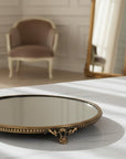 Decorative round mirror with brass frame on a marble surface, blurred chair and mirror in the background