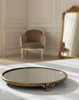 Decorative  brass round mirror tray with  frame on a table in a room with a chair and mirror.