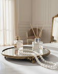 Two glass diffusers on a round mirror brass tray with pearls in a room setting.