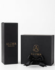 Two black ALUMA fragrance boxes on a white background, one tall rectangular box and one square gift box with a black ribbon bow, both featuring gold lettering.
