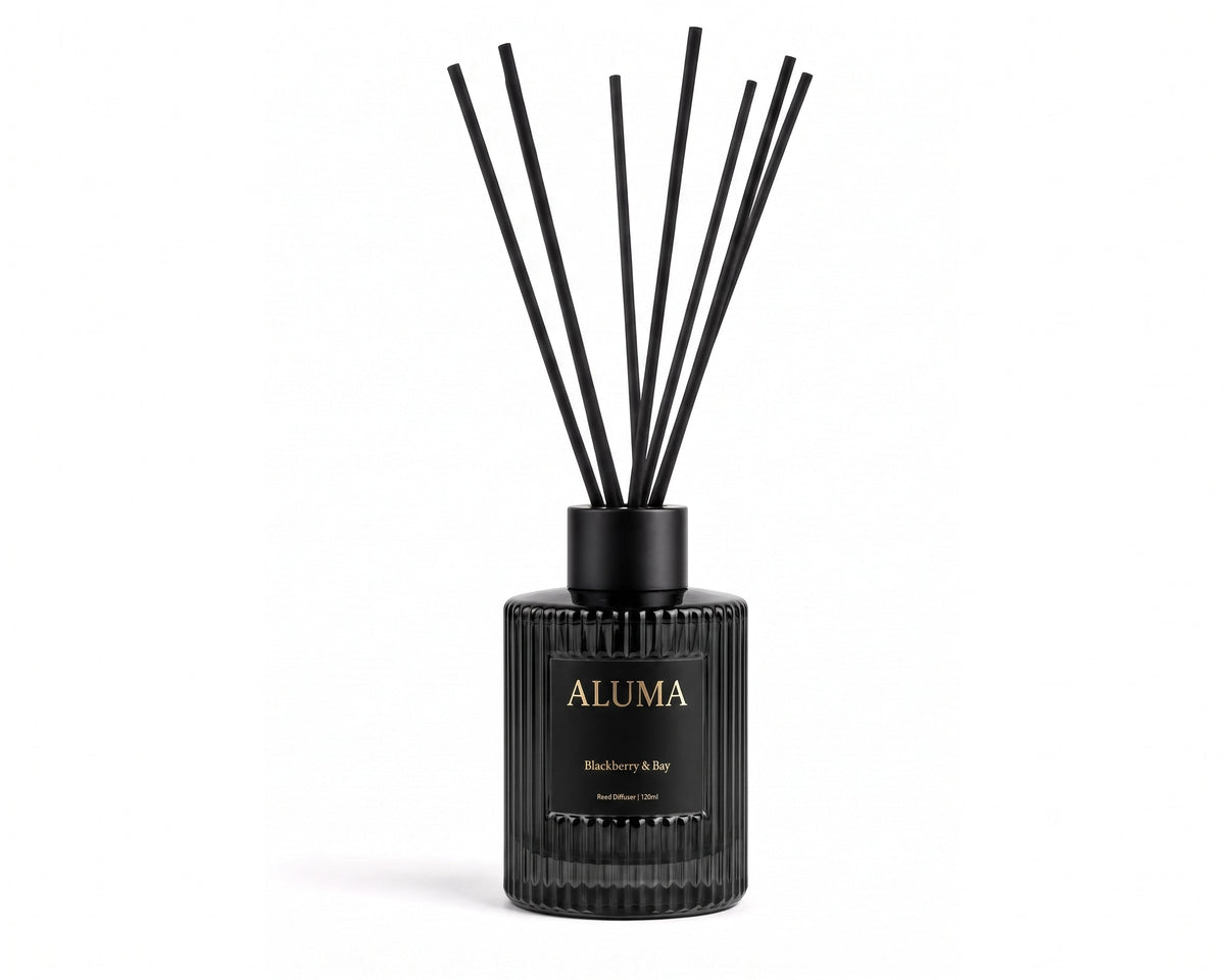 A reed diffuser bottle in a textured black glass with black reeds, featuring a black label with gold lettering that reads 'ALUMA' and 'Blackberry & Rose London Air'.