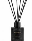 A reed diffuser bottle in black ribbed glass with black reeds, featuring a black label with gold lettering that reads 'ALUMA' and 'Blackberry & Bay'.