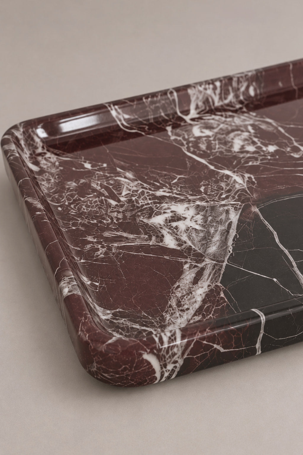 A rectangular marble tray with rounded corners, featuring a dark reddish-brown and black marble pattern with white veining, photographed on a neutral beige background.