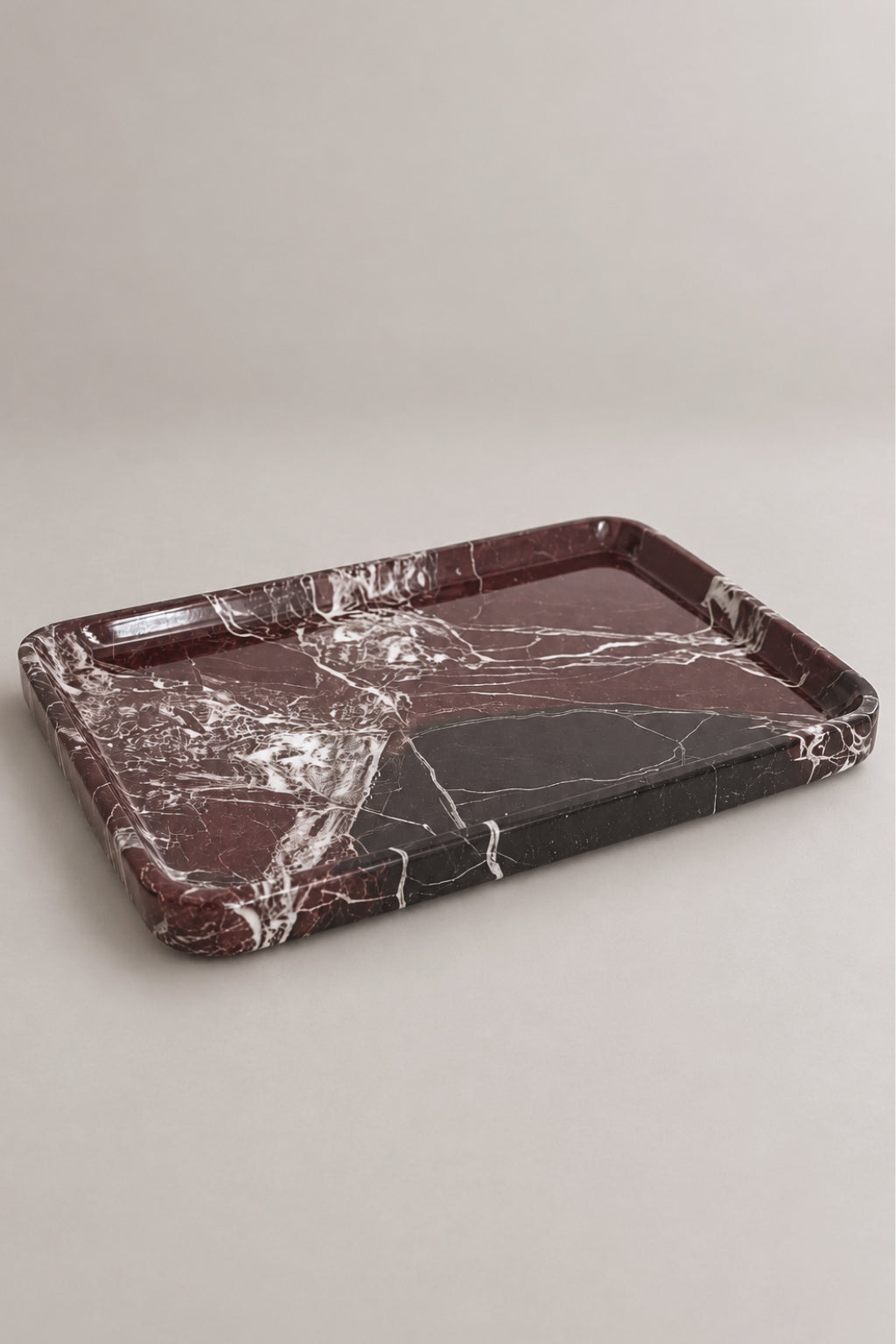 A rectangular marble serving tray with a deep rim, featuring a dark reddish-brown and black marble pattern with white veining, set against a neutral light gray background.
