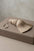 A beige decorative curtain tassel with a braided top and loop, resting on a matching taupe leather box against a neutral textured background.