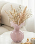 Pink vase with dried flowers on a white surface with a blurred background
