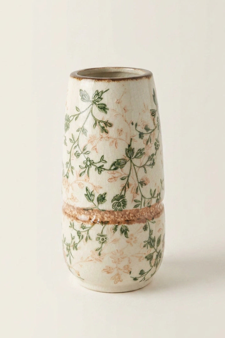 A small cylindrical ceramic vase with a textured off-white glaze, decorated with green botanical vines and delicate peach-pink floral motifs, separated by a rustic terracotta band.